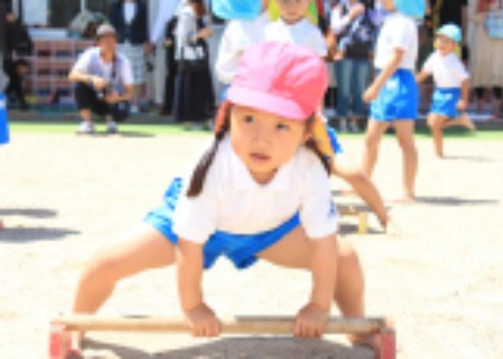 園庭で低い器具に両手をつき、体を動かす子ども