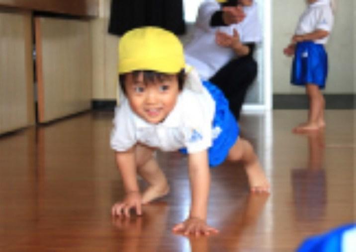 室内で両手を床につき、手足で体を支える子ども