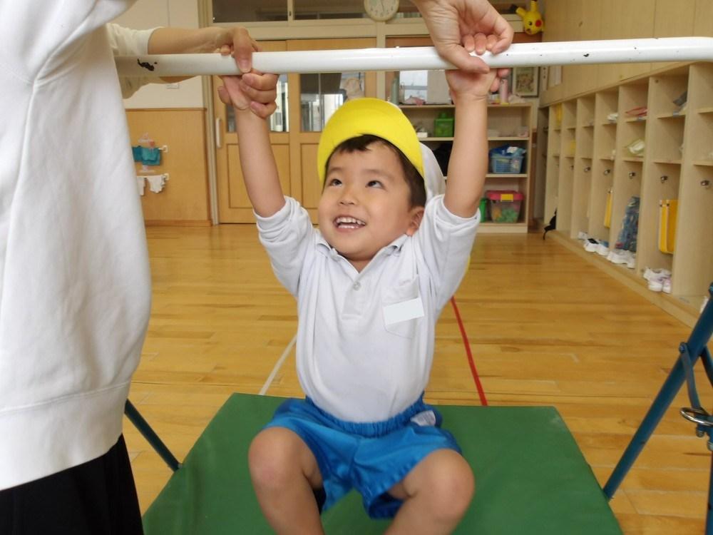 鉄棒にぶら下がる子どもを、先生が両手で支えている場面