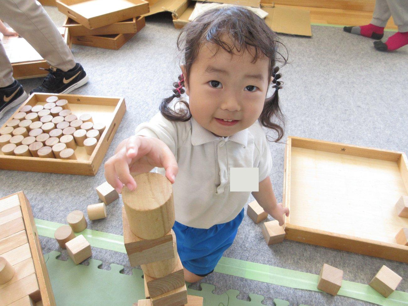積木教室で、木の積木を高く積んでいる場面。