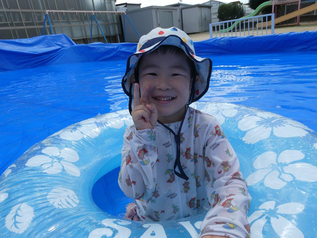 園庭に設けられたプールで、水遊びを楽しんでいる場面。